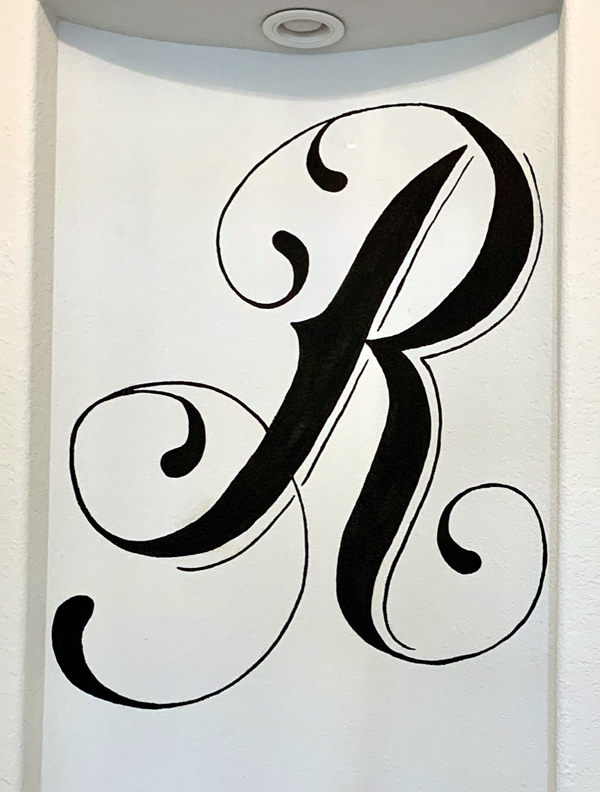 A painted monogram of the letter R on a wall in a home.
