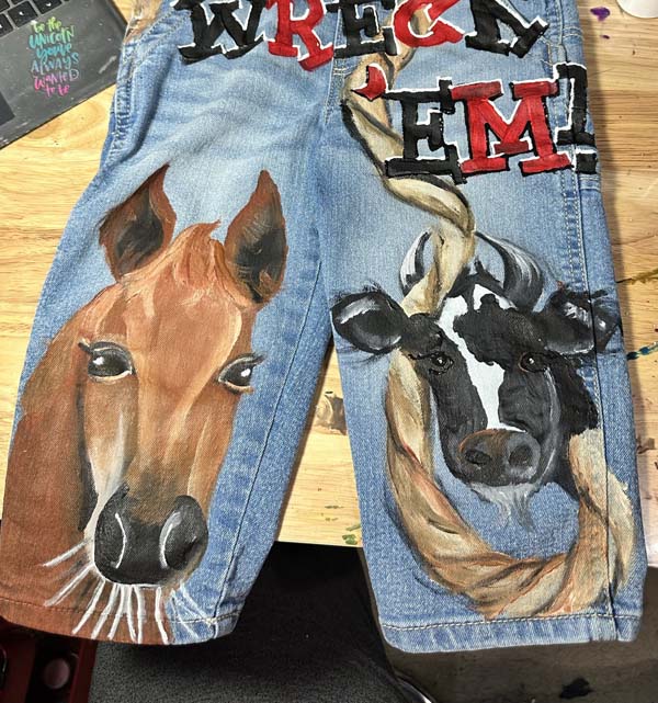 detail of front of rodeo overalls with a hand painted horse and cow and rope